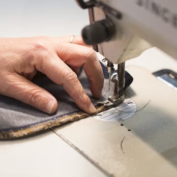 Home 5 Tailor guiding fabric through a sewing machine during clothing alterations